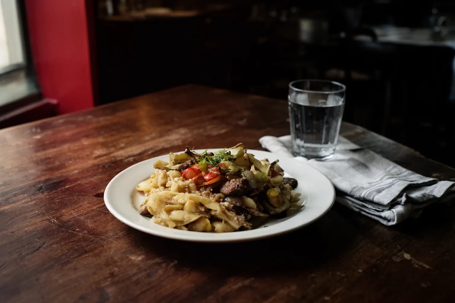 Assiette du plat du jour sur une table de bistrot en bois usé, dans la lumière d’une fenêtre