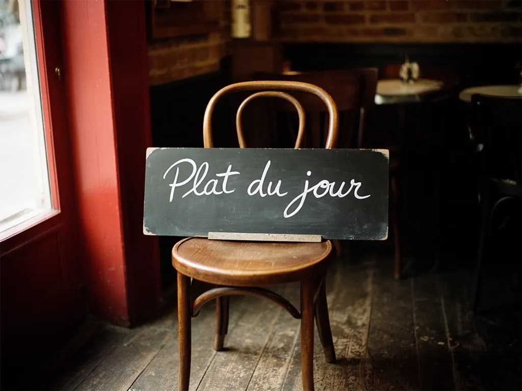 Ardoise du plat du jour écrite à la craie, posée sur une chaise de bistrot près de la porte